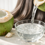 Fresh green coconut cut open with clear coconut water being poured into a glass bowl, natural shiny hair texture in the background under soft daylight.