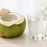 Fresh green coconut cut open with clear coconut water poured into a transparent glass, placed on a clean white surface in soft natural light